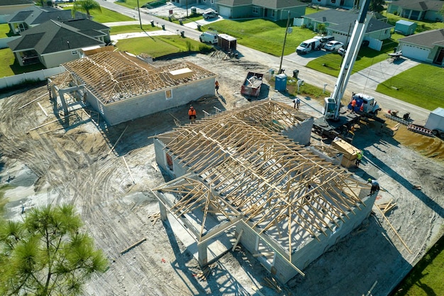 Luchtfoto van hijskraan en bouwers die werken aan een onvoltooid woonhuis met houten dakframeconstructie in aanbouw in de buitenwijken van Florida