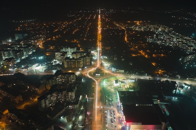 Luchtfoto van hoogbouw appartementsgebouwen en helder verlichte rotonde kruising op stedelijke straat in de woonwijk van de stad 's nachts. Donker stedelijk landschap.