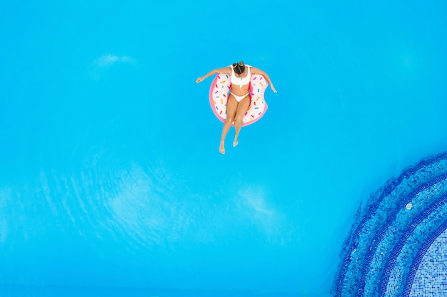 Luchtfoto van jonge mooie meisje in een witte bikini ontspannen op opblaasbare donut in het zwembad. zomervakantie achtergrond