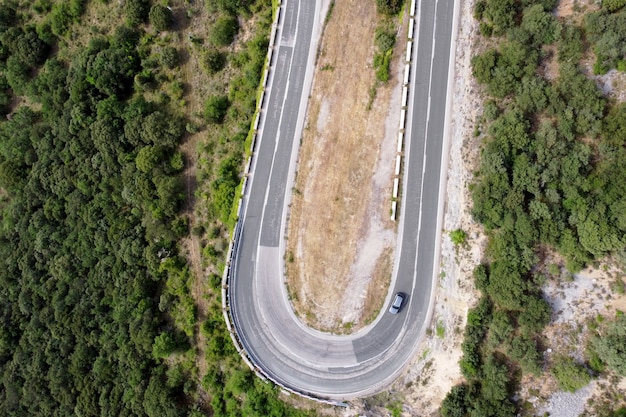 Luchtfoto van kronkelende weg in hoge bergpas via groene dennenbossen.