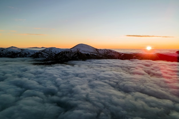 Luchtfoto van levendige zonsopgang boven witte dichte mist met verre donkere bergen aan de horizon.