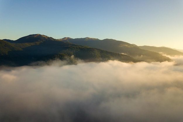 Luchtfoto van levendige zonsopgang boven witte dichte mist met verre donkere silhouetten van bergheuvels aan de horizon