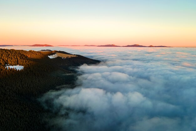 Luchtfoto van levendige zonsopgang boven witte dichte wolken met verre donkere bergen aan de horizon.