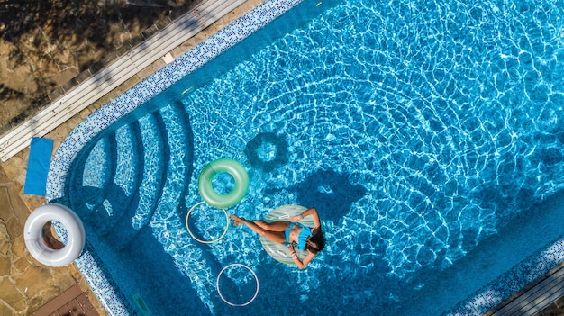 Luchtfoto van mooi meisje in zwembad van bovenaf, zwemmen op opblaasbare ringdoughnut en heeft plezier in water op familievakantie op tropisch vakantieoord