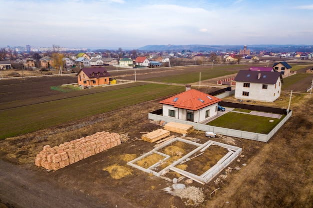 Luchtfoto van nieuw huis dak met zolder ramen en bouwplaats, fundering van toekomstige huis, stapels bakstenen en bouw houtblokken voor de bouw.