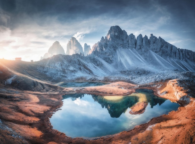 Luchtfoto van prachtige rotsen bergmeer weerspiegeling in water en huizen op de heuvel bij zonsondergang Zomerlandschap met bergen blauwe lucht en zonlicht Dolomieten Italië Bovenaanzicht van Italiaanse Alpen