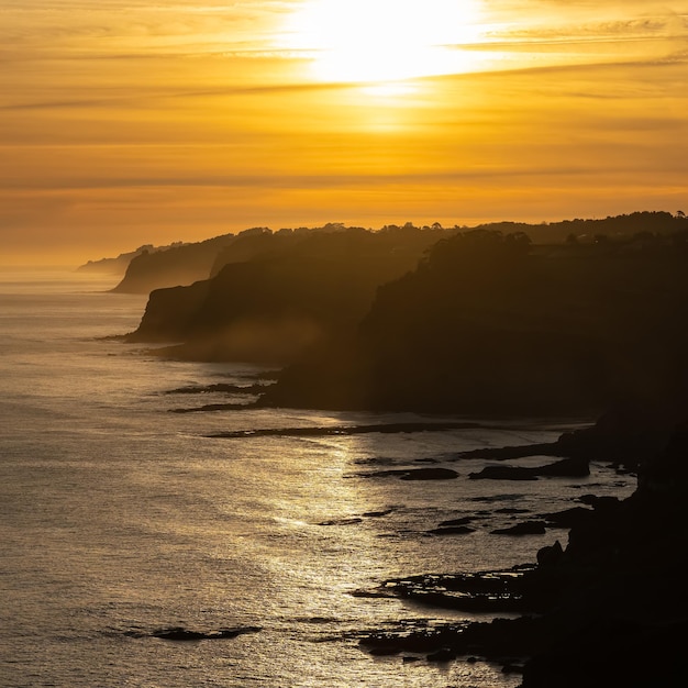 Luchtfoto van rotswanden in de zee terwijl de zon ondergaat achter het lichte Asturias Spanje