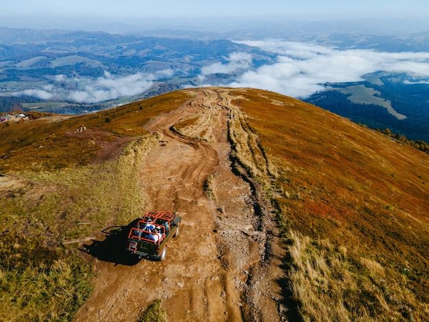 Luchtfoto van suv off-road reizen die omhoog klimt door bergheuvel kopieer ruimte herfstseizoen boven de wolken