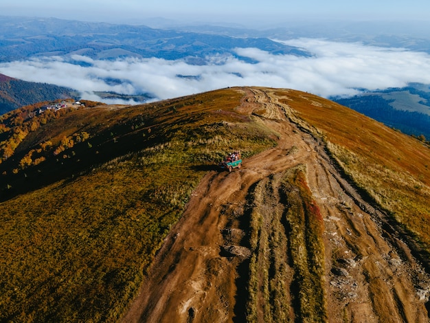 Luchtfoto van suv off-road reizen klimmen door bergheuvel kopieer ruimte herfstseizoen boven de wolken