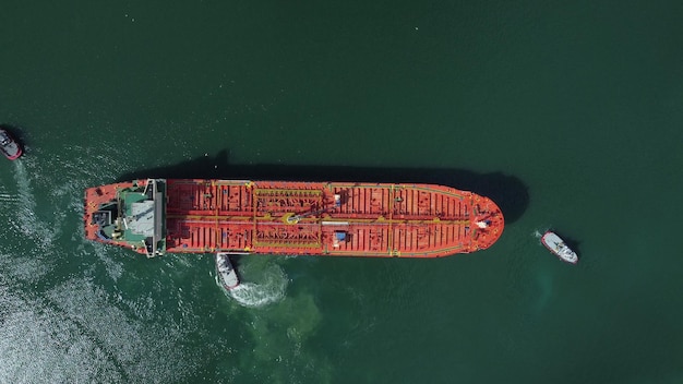 Luchtfoto van tankschip met begeleidende sleepboot die de haven verlaat