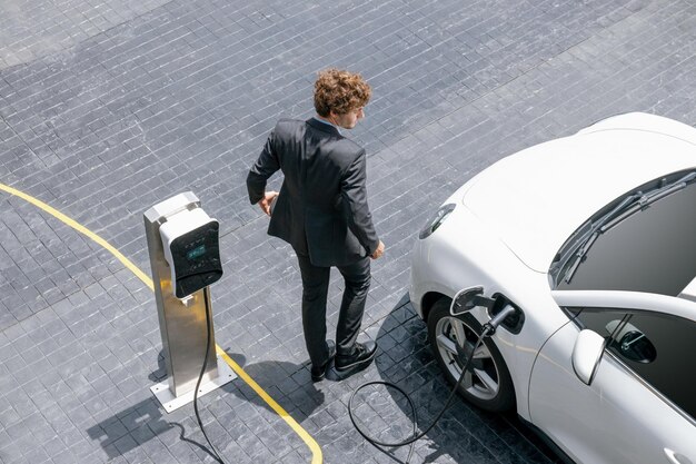 Luchtfoto van vooruitstrevende zakenman met EV-auto die batterij oplaadt