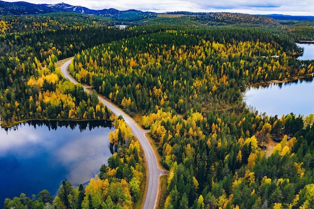 Luchtfoto van weg en kleurrijk herfstbos met bergen en blauwe meren in Finland Lapland