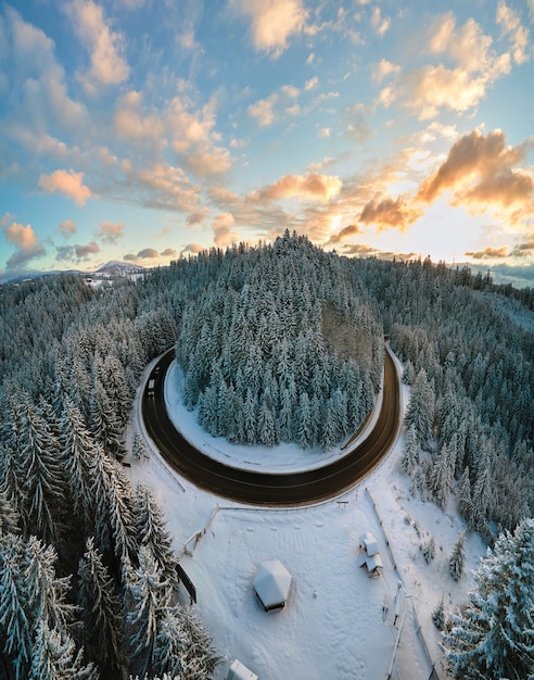 Luchtfoto van winterlandschap met besneeuwde bergheuvels en kronkelende bosweg in de ochtend.