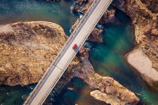 Luchtfoto van witte brug met bewegende rode auto over blauw water en steenachtige eilanden.