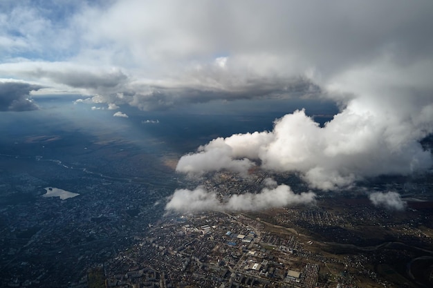 Luchtfoto vanuit het vliegtuigraam op grote hoogte van een verre stad bedekt met gezwollen cumuluswolken die zich vormen vóór een regenbui