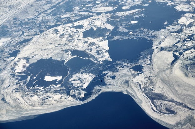 Luchtfoto vanuit vliegtuigraam over wolken boven naar besneeuwde bevroren zee winter verse ijzige lucht