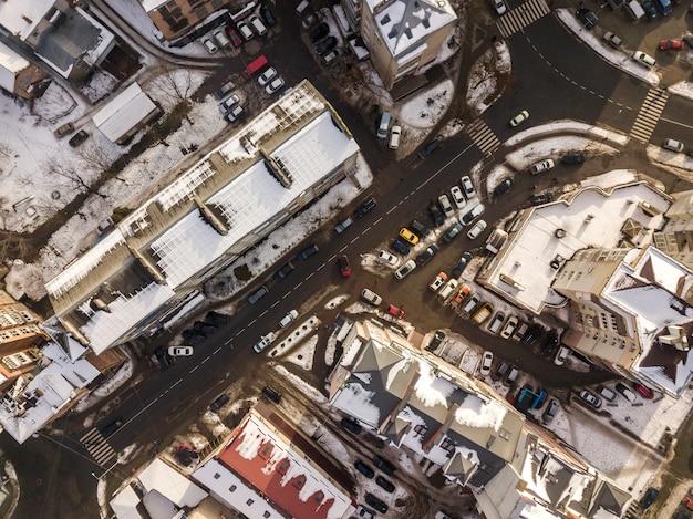 Luchtfoto zwart-wit winter bovenaanzicht van moderne stad met hoge gebouwen, geparkeerde en rijdende auto's langs straten met wegmarkering.