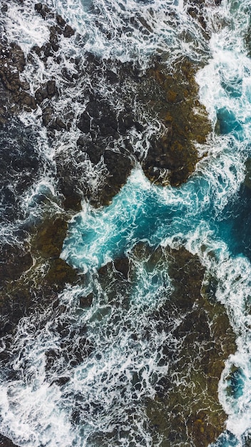 Luchtfotografie van golven die op rotsen beuken