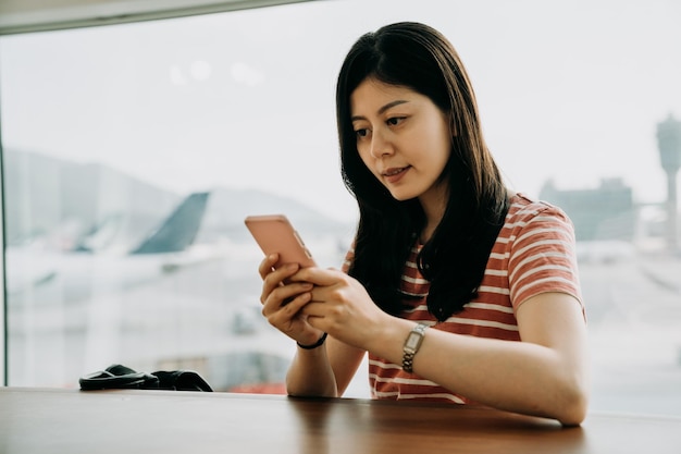 Luchthaven telefoon reizen vrouw met behulp van mobiele telefoon in business class lounge wachten op vertraging vliegtuig vlucht sms-bericht op smartphone. Technologie en reizen mensen frequente vliegende levensstijl.