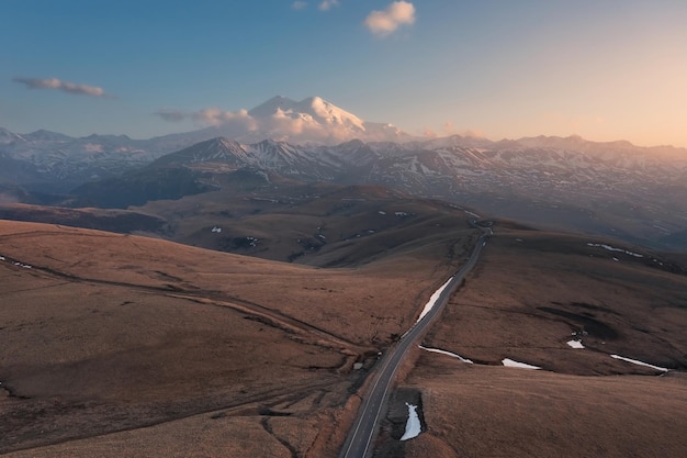 Luchtlandschap met weg langs heuveltoppen naar besneeuwde hoge berg MtElbrus, Rusland