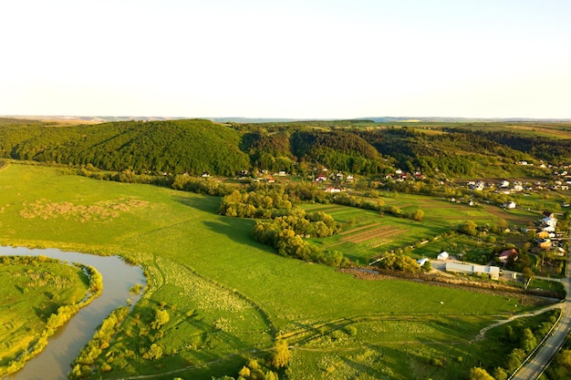 Luchtlandschapsmening van groene gecultiveerde landbouwgebieden met groeiende gewassen en verre dorpshuizen op heldere zomer.