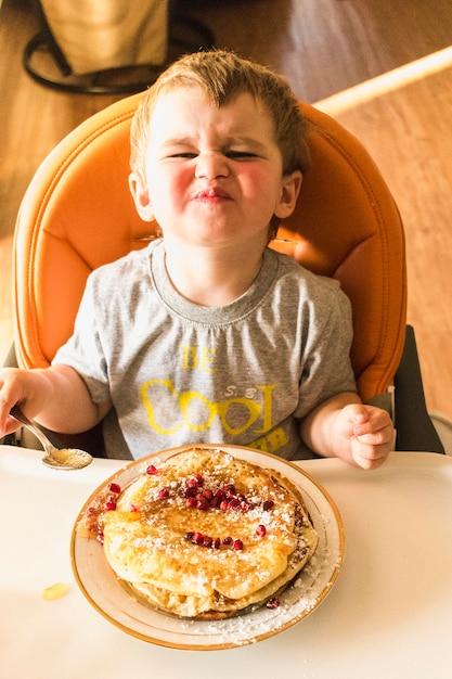 Foto luchtmening van babyjongen die terwijl het eten van pannekoek steenbolk pruilen