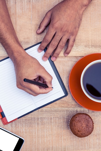 Luchtmening van de mens die op agenda bij lijst door koffie en kopcake schrijven