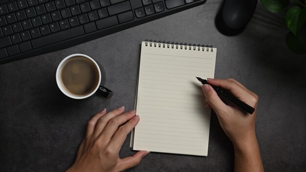 Luchtmening van de mensenhand die pen houden en op leeg notitieboekje schrijven