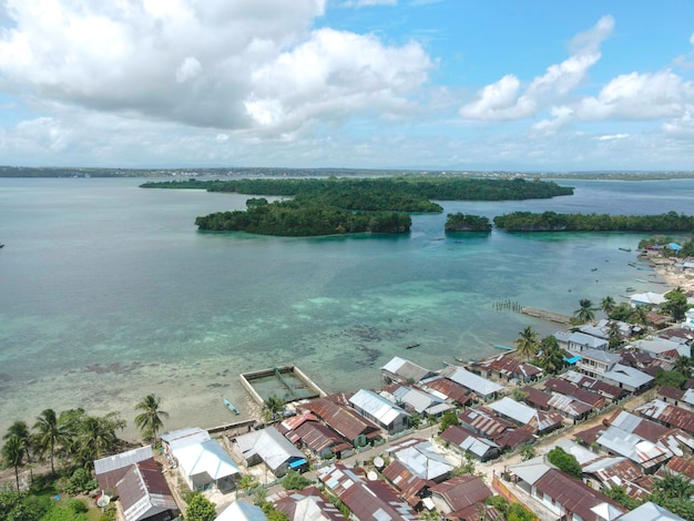 Luchtmening van dorp dichtbij mooi strand met klein eiland op de achtergrond in Maluku, Indonesië