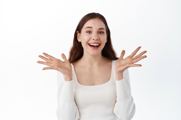 Lucky beautiful girl rejoicing from good news, laughing and smiling, raising hands up to celebrate joyful positive moment, hear good news, standing against white wall