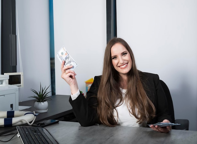 Donna bionda fortunata con in mano banconote da 100 dollari entusiasta di vincere un premio in denaro che esprime vittoria e ricchezza donna con denaro contante in banconote in dollari in mano donna con capelli lunghi che tiene banconote