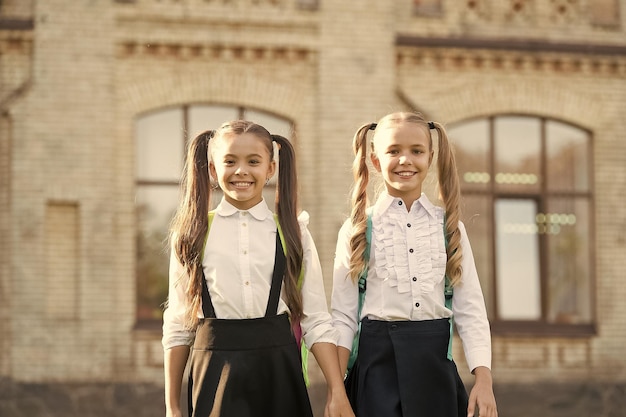 Fortunati ad incontrarsi studentesse intelligenti e allegre studentesse felici all'aperto le piccole studentesse indossano l'uniforme scolastica studentesse carine con lunghe code di cavallo che sembrano affascinanti fine dell'anno scolastico