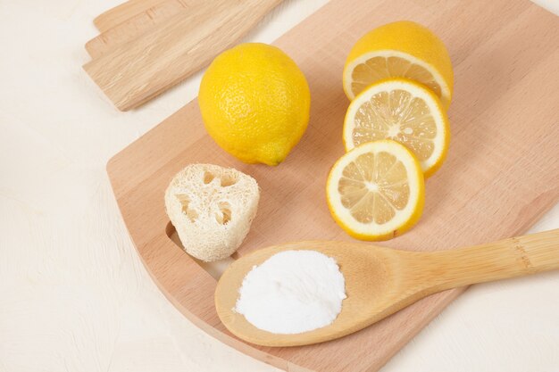 Luffa, lemon and baking soda on wooden spoon, knitting board on beige background copy space eco cleaning concept