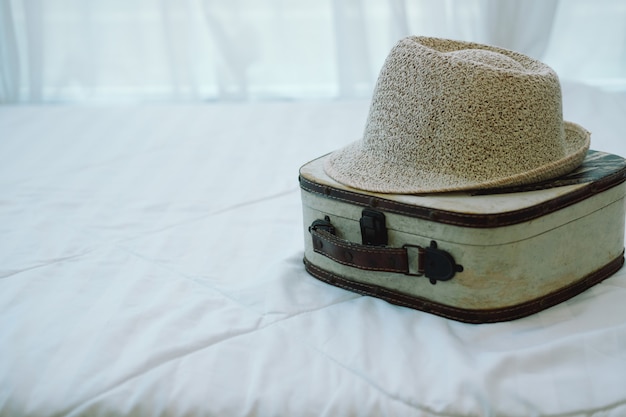 Luggage and hat on white bed mattress