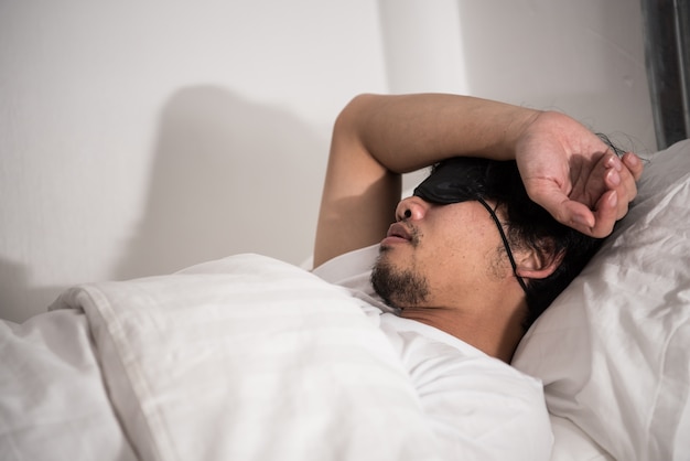 Luiheid van de Aziatische man die nog steeds op het bed in de slaapkamer in de ochtend slaapt