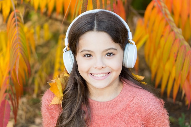 Luisteren lied Geniet van muziek buitenshuis, herfst warme dag Audiobestand Educatieve podcast Herfst afspeellijst concept Voel vreugde Kid meisje ontspannen in de buurt van herfst boom met koptelefoon Muziek voor herfst gezellige sfeer