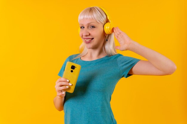 Luisteren naar muziek met een koptelefoon online blond blank meisje in de studio op gele achtergrond