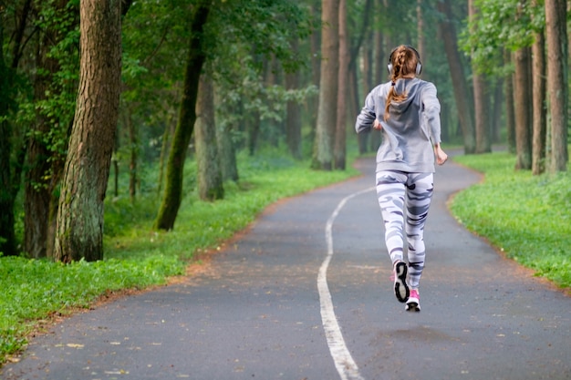 Luistert de roodharige sportieve jonge vrouw in het park en luistert muziek