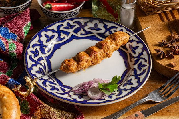 Photo lula - kebab made of finely chopped lamb cooked on the grill with red onion and parsley on a plate with traditional uzbek ornaments