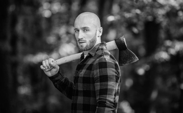 Lumberjack carry ax. bald woodsman. harvest firewood. hike\
vacation. hike in forest. forest care. determination of human\
spirit. man checkered shirt use axe. brutal male in forest. power\
and strength.