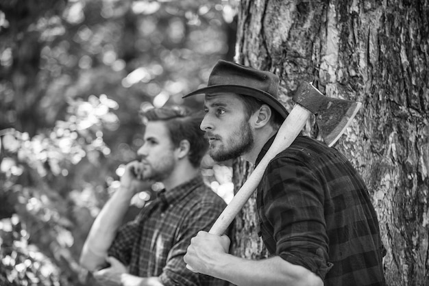 Lumberjack with chainsaw and ax Harvest firewood hiking in deep wood forest care at vacation summer or spring activity man relax in forest rangers use lumberjack equipment What a great day