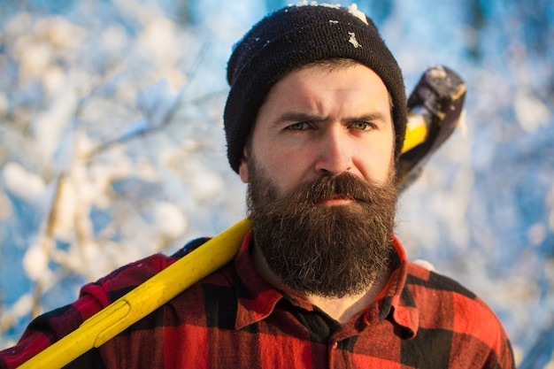 Lumberjack in the woods with an ax. Brutal bearded man with beard and moustache on winter day, snowy forest. Handsome man, hipster, lumberjack. Attractive bearded male outdoors in winter.