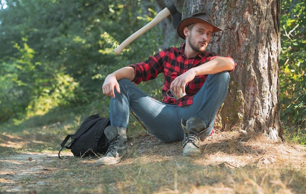 Lumberjack worker man sitting in the forest lumberjack with axe on forest background man doing mans