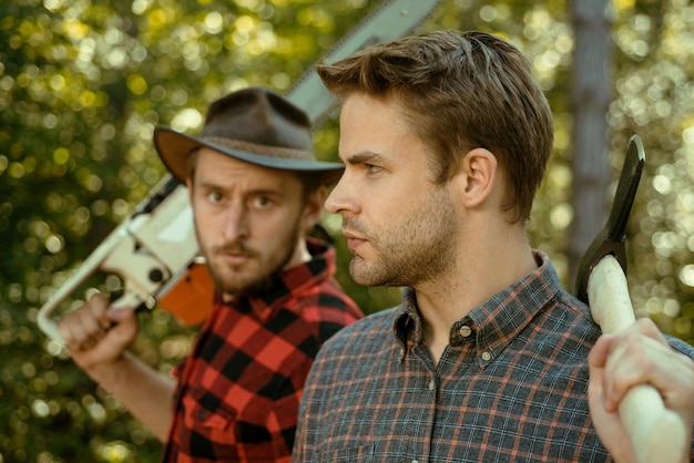 Lumberjack workers in the forest woodcutter with axe and lumberjack with chainsaw handsome woodcutte