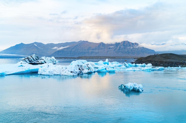 氷河の山を背景にしたヨークルスアゥルロゥン氷河ラグーンに浮かぶ明るい青い氷山。南アイスランド、vatnajã¶kull国立公園。スペースの背景をコピーします。テキストの場所。