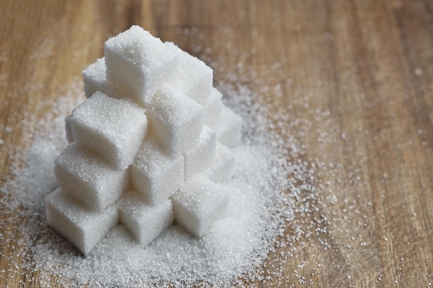 写真 木製のテーブルにピラミッド状に積み上げられた砂糖の塊木製の表面に散らばった砂糖精製された砂糖
