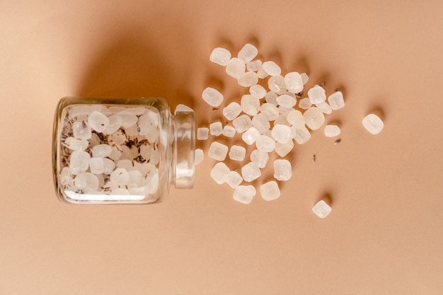 Lumps of sugar mixed with lavender fall out of a glass jar on a beige background