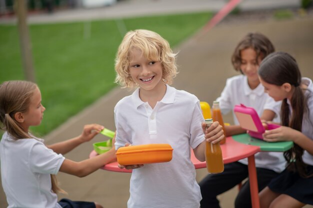 Lunch. A blonde boy with a lunch box smiling positively