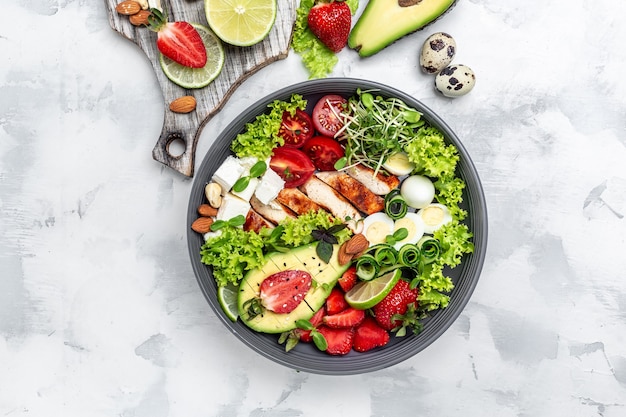 Lunch bowl with chicken, avocado, feta cheese, quail eggs, strawberries, nuts and lettuce. Detox and healthy superfoods bowl concept. top view.