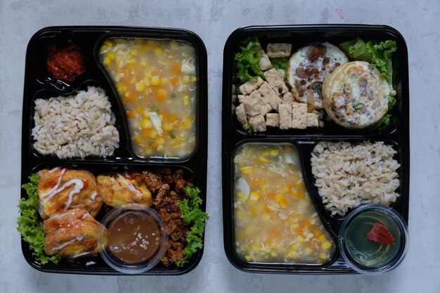 lunch box of healthy food bento with brown rice, scrambled egg, corn soup, tempeh tofu. diet menu.